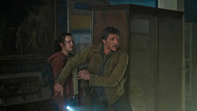 A promo image with Pedro Pascal and Bella Ramsey in HBO's The Last of Us. The two huddle in a dark corner of the room with a single flashlight, worried about some danger in the vincinity.