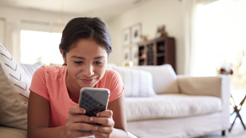 Teenage girl lying on the sofa at home in the living room using smartphone, close up, low angle, close up