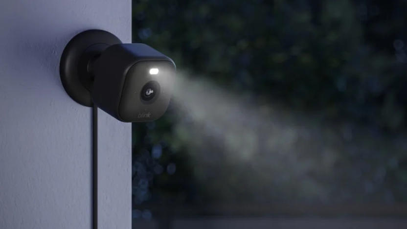 The new Blink Mini 2 camera in black shown mounted to an outside wall at nighttime with the LED spotlight shining