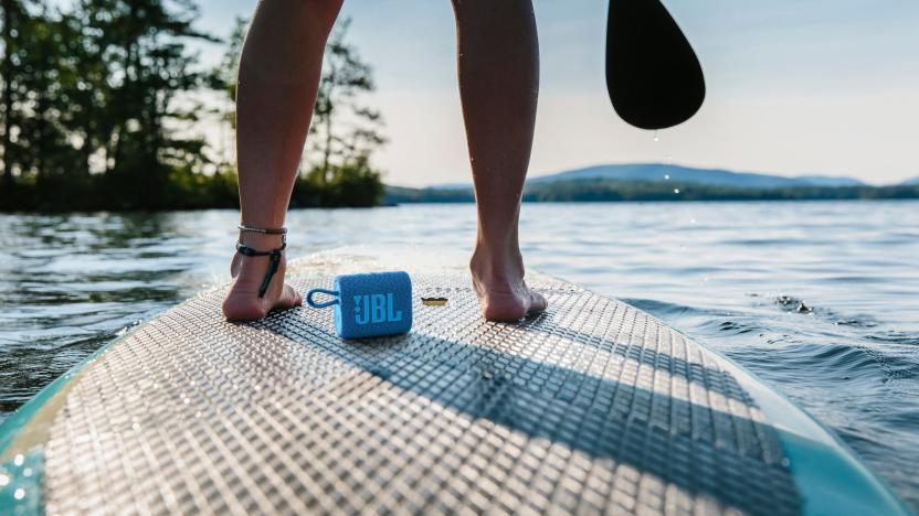 Product photography of JBL Go 3 Eco on a surfboard between a rider's feet.