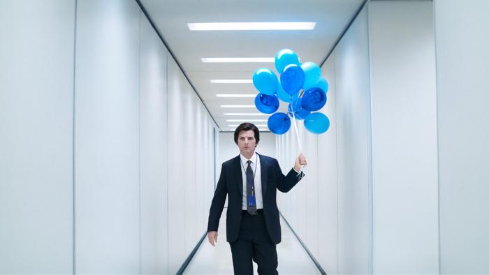 Adam Scott (wearing a suit) holds a bunch of blue blues in a white hallway in Severance.