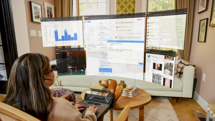 A woman uses Spacetop in her living room, which displays virtual computer desktop windows on a curved space in front of here via Augmented Reality (AR) glasses.