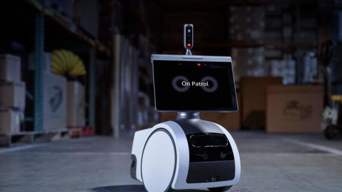 Security robot (screen with wheels and a periscope) sitting in a dark warehouse.