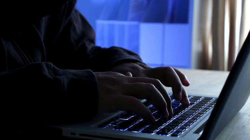 Hacker working on laptop at night under blue light.