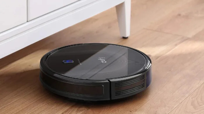 the eufy BoostIQ RoboVac 11S MAX robot vacuum is running on a hardwood floor and about to clean under a cabinet. 