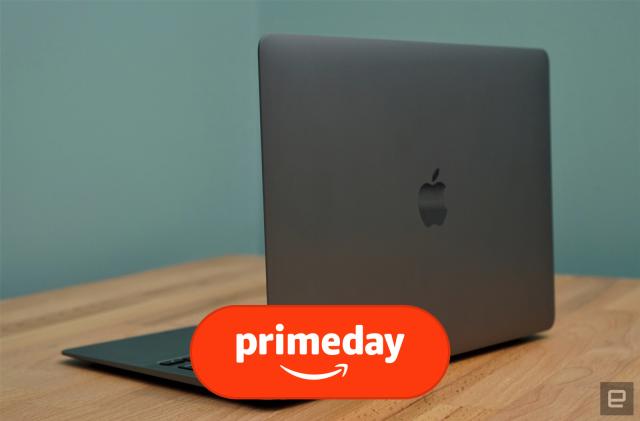 A silver MacBook Air laptop sits on a brown desk in front of a blue wall, with its back facing the camera at an angle, showcasing an Apple logo.