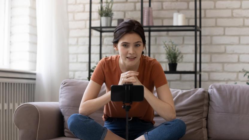 Vlogger influencer. Young woman blogger sitting cross-legged on sofa at home recording clip content to channel. Inspired millennial female speaking to audience followers making viral video review