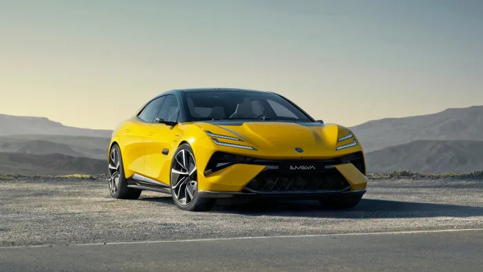 A Lotus Emeya EV in yellow is parked by the side of a desert road with low hills in the distance.