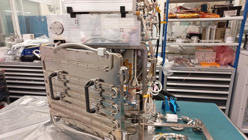 A raw metal 3D printer with lots of stainless steel and tubing that will be tested on the International Space Station sits on a cluttered workbench in a lab.