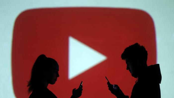 Silhouettes of mobile users are seen next to a screen projection of Youtube logo in this picture illustration taken March 28, 2018.  REUTERS/Dado Ruvic/Illustration