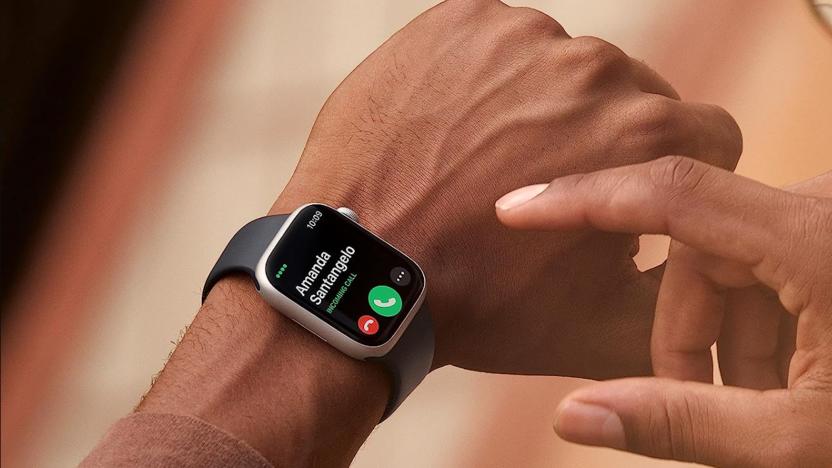 The Apple Watch 8 is seen being worn on a wrist while the other hand aims to poke at an onscreen icon in this cropped photo.