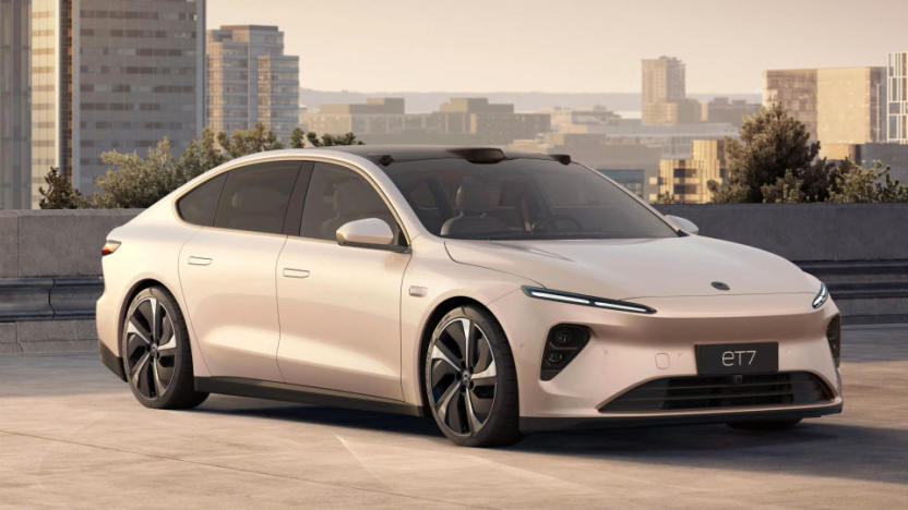 Marketing image of the Nio ET7 EV. The goldish-beige car sits on a lot overlooking a city skyline during daytime.