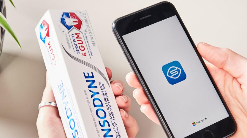 Close-up of a person’s hands holding a box of Sensodyne toothpaste in one hand and a phone displaying the Seeing AI app in the other.