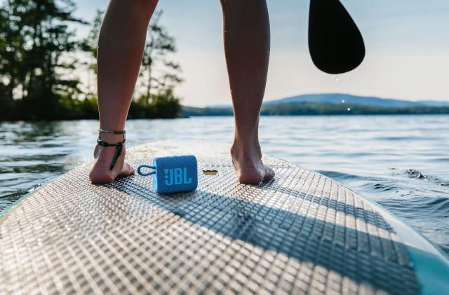 Product photography of JBL Go 3 Eco on a surfboard between a rider's feet.