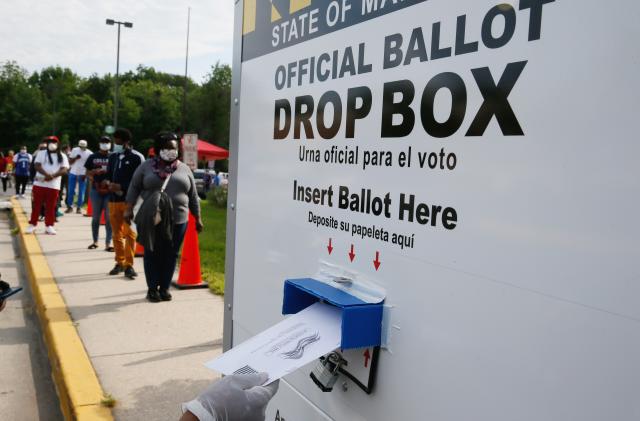A voter places their ballot in a curbside ballot drop box to help prevent the spread of coronavirus disease (COVID-19) during the Maryland U.S. presidential primary election as other voters stand in a long line waiting to cast their votes in College Park, Maryland, U.S., June 2, 2020. REUTERS/Jim Bourg