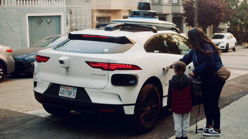 A woman and a child and are standing next to a white autonomous vehicle, in the process of pulling a door open. 