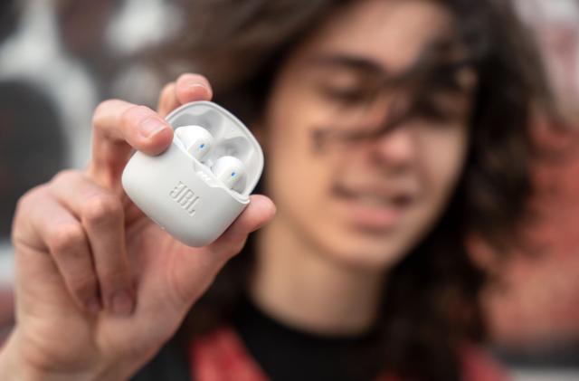 A young man holding white JBL Tune Flex earbuds.