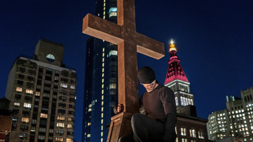 Daredevil looks down on the city from his perch holding onto a cross at the top of a church.