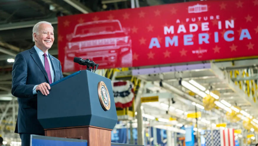 President Joe Biden standing at a podium in an auto factory. A sign behind says "A Future Made in America."