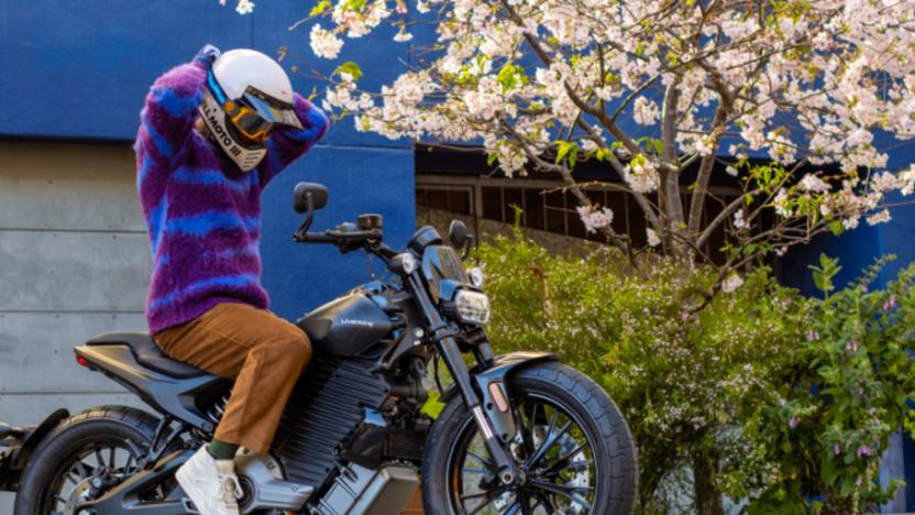 A person fixes their helmet while on a LiveWire S2 Del Mar electric motorcycle.