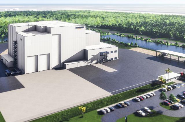 Rendered photo of Amazon’s satellite-processing facility for its Project Kuiper satellite broadband initiative. A large light-colored building with an Amazon logo sits next to a large lot. It’s surrounded by a parking lot (full of cars) with water and trees in the background.