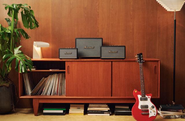 A living room media console has three Marshall speakers on it, with records in the cabinet and a guitar leaning against it.