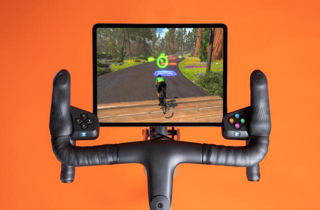 Zwift Play controllers attached to handlebars with a tablet running a cycling game. 