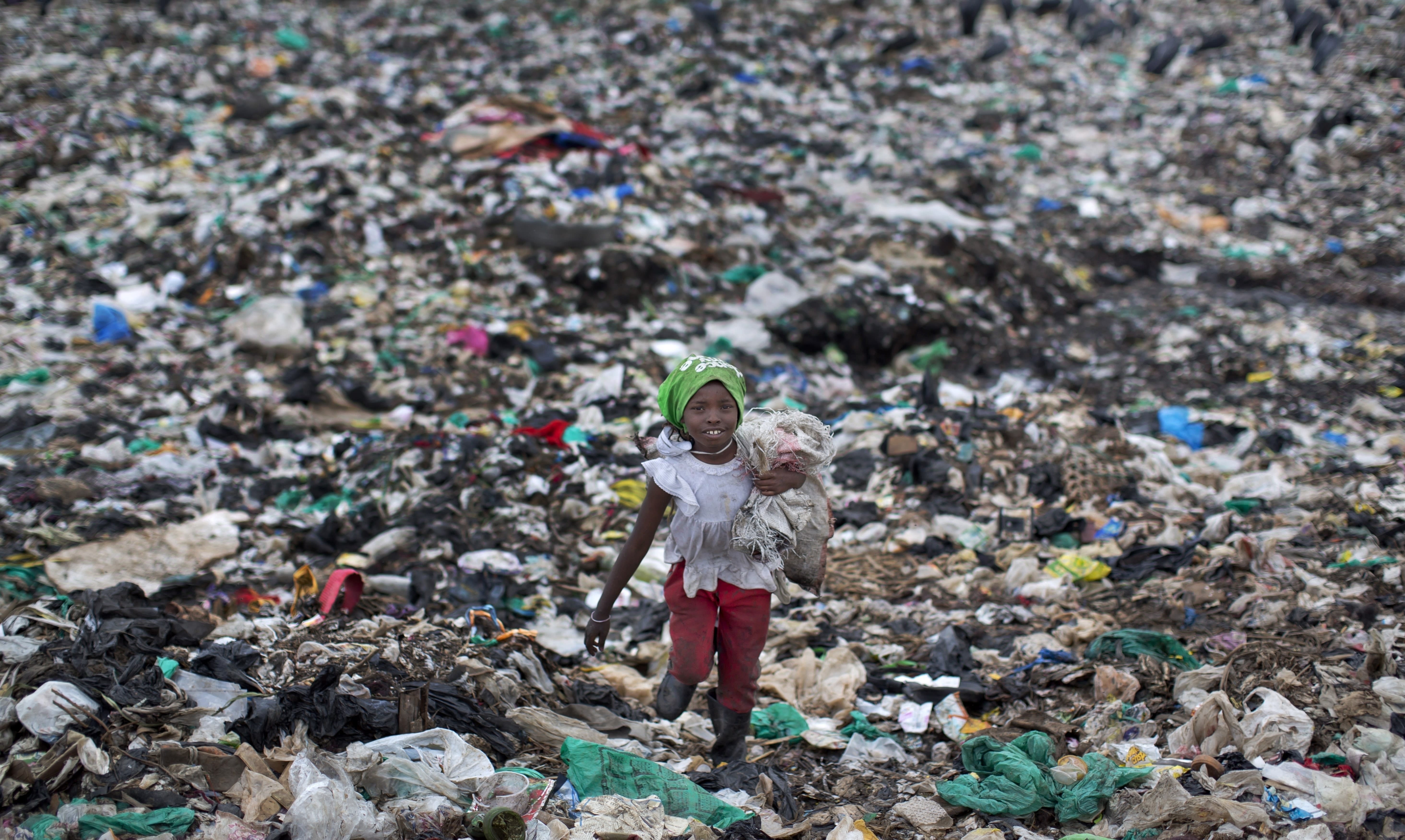 FILE - In this Thursday, Nov. 12, 2015 file photo, Joyce Njeri, 8, carries a torn sack holding the plastic bottles she has scavenged, as she walks amidst garbage and plastic bags at the garbage dump in the Dandora slum of Nairobi, Kenya, before a ban on plastic bags came into force in Kenya in 2017. The oil industry in 2020 has asked the United States to pressure Kenya to change its world-leading stance against the plastic waste that litters Africa, according to environmentalists who fear the continent will be used as a dumping ground. (AP Photo/Ben Curtis, File)