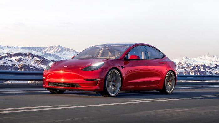 Marketing image for the Tesla Model 3. The red car drives on an open highway with snowy mountains in the background.