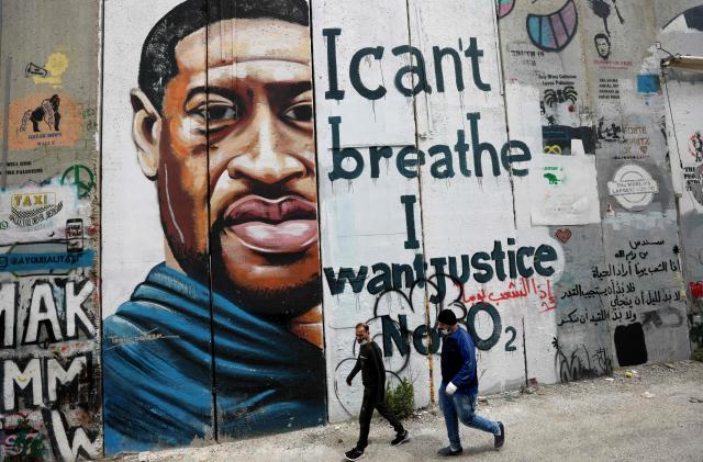 People walk past a mural showing the face of George Floyd, an unarmed handcuffed black man who died after a white policeman knelt on his neck during an arrest in the US, painted on a section of Israel's controversial separation barrier in the city of Bethlehem in the occupied West Bank on March 31, 2021. - The teenager who took the viral video of George Floyd's death said on March 30, at the trial of the white police officer charged with killing the 46-year-old Black man that she knew at the time "it wasn't right." Darnella Frazier, 18, was among the witnesses who gave emotional testimony on Tuesday at the high-profile trial of former Minneapolis police officer Derek Chauvin. Chauvin, 45, is charged with murder and manslaughter for his role in Floyd's May 25, 2020 death, which was captured on video by Frazier and seen by millions, sparking anti-racism protests around the globe. (Photo by Emmanuel DUNAND / AFP) (Photo by EMMANUEL DUNAND/AFP via Getty Images)