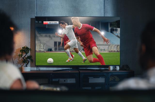 Black Couple Watches Professional Soccer Match on TV, Sitting on a Couch at Home in the Evening. Boyfriend and Girlfriend Football Fans Watch Sports. Back View Out of Focus Close Up Shot at Night.