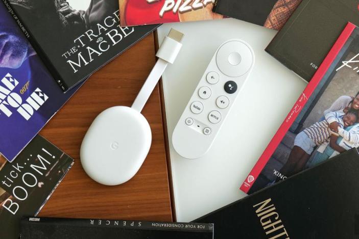 Review photo of the Chromecast with Google TV (HD). The streaming dongle and remote sit on a desk, surrounded by books.