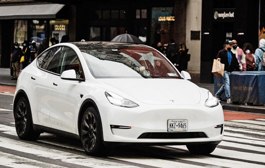 A white Tesla Model 3 crosses a crosswalk in the road in New York City.