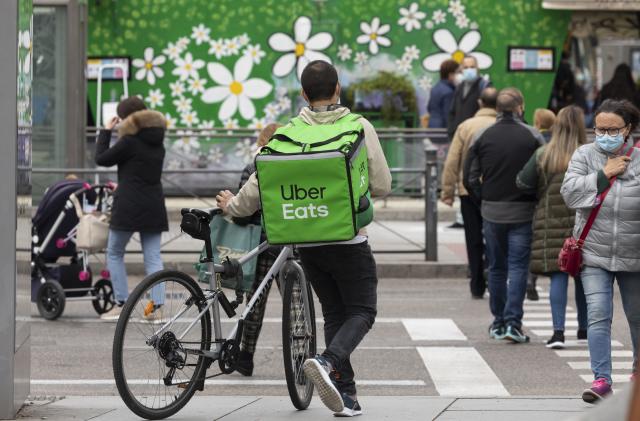 Madrid, Spain - Nov 25, 2020: A worker, a food delivery delivery man for the Uber Eats company, walks with his bicycle and crosses Narvaez street