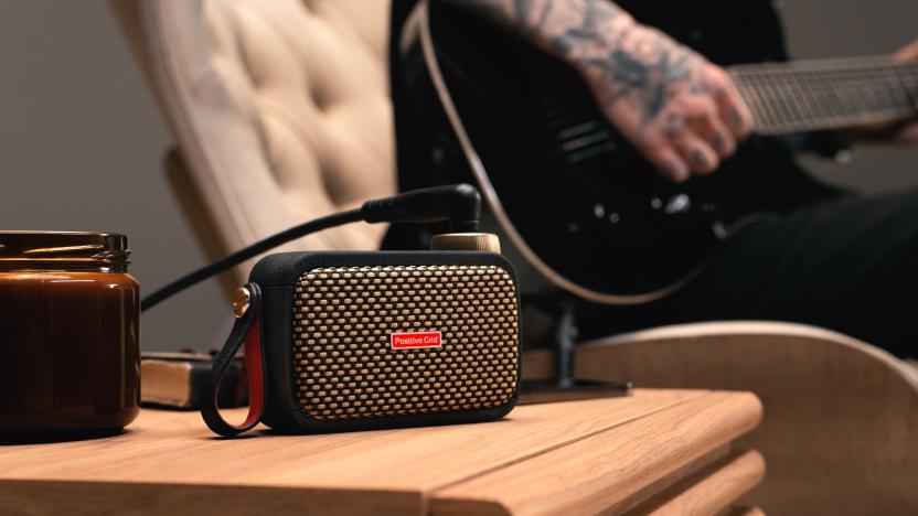 Positive Grid's Spark Go mini-amp, sitting on a table net to a person strumming a connected electric guitar.