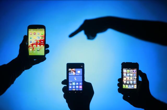 Men are silhouetted against a video screen as they pose with Samsung Galaxy S3, Nokia Lumia 820 and iPhone 4 smartphones (L-R) in this photo illustration taken in the central Bosnian town of Zenica, May 17, 2013. REUTERS/Dado Ruvic (BOSNIA AND HERZEGOVINA - Tags: BUSINESS TELECOMS)