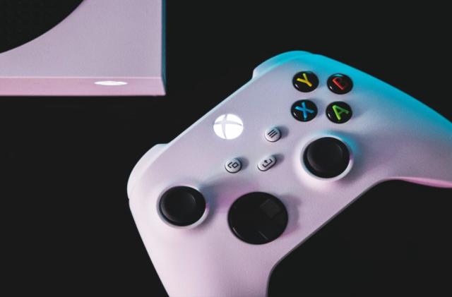 A white Xbox Wireless Controller displayed against a black background next to an Xbox Series S.