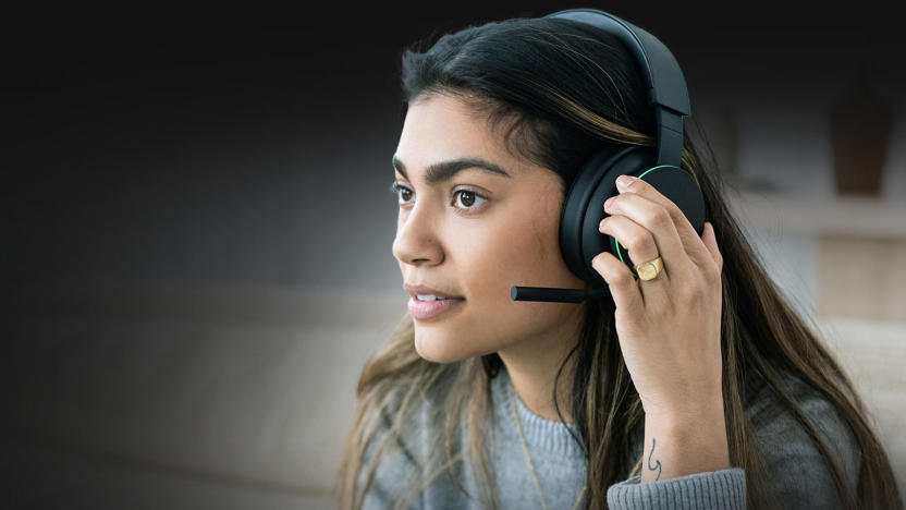 Marketing photo for the Xbox wireless headset. A young woman wears the black over-ear headset with protruding mic. She faces the left with her left hand over the ear cup. She has a calm but determined look on her face.