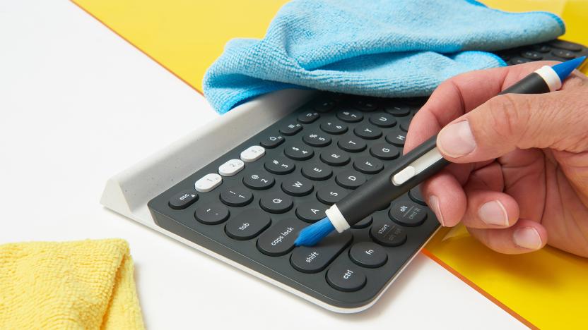 A wireless keyboard is being cleaned by a brush with clothes scatter in the background.