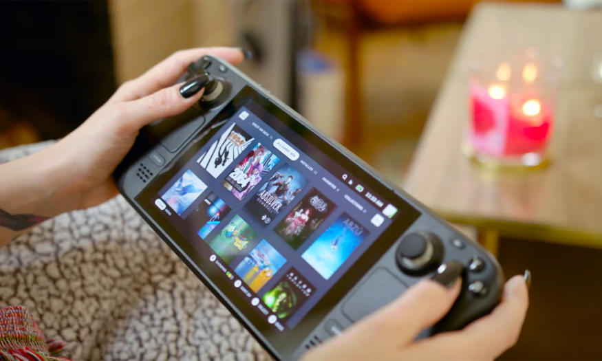 A cropped image showing someone holding a Valve Steam Deck handheld gaming console in their lap while on a living room couch.