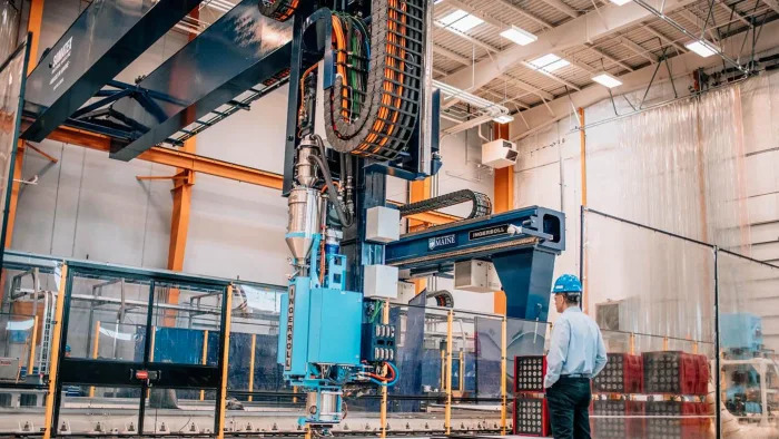 A man stands next to a giant 3D printer.