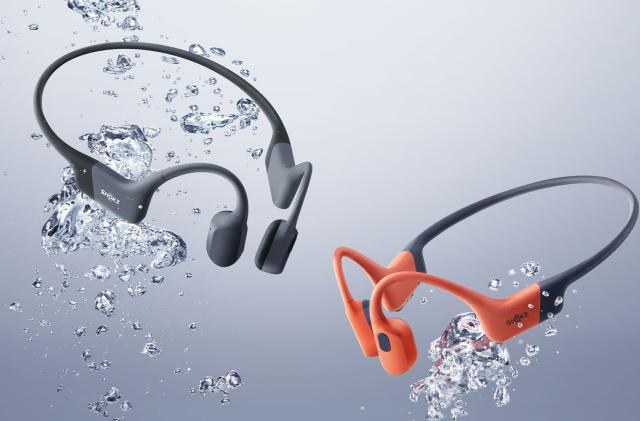 Two Shokz OpenSwim Pro headsets are shown surrounded by watery bubbles as if they were submerged in water.