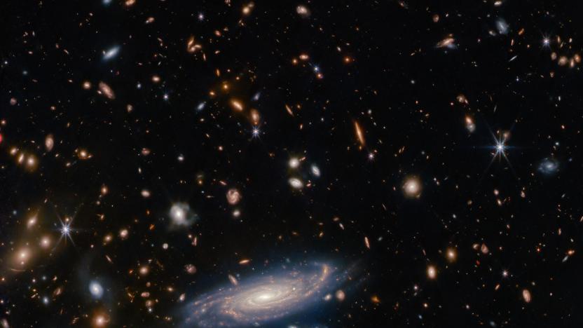 Image that was taken with the James Webb Space Telescope showing a spiral galaxy at the bottom center, surrounded by more distant galaxies (appearing as blobs) and individual stars.