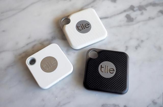 Three Tile trackers on a granite countertop in a triangular pattern. Two of them are white and one is black.