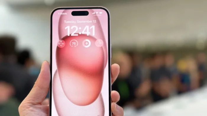 A pink iPhone 15 held in mid-air with its screen facing the camera.  