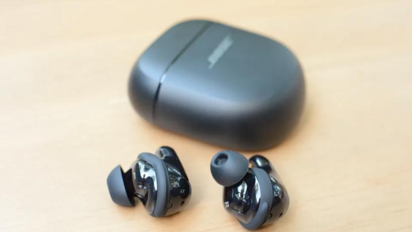 A pair of earbuds on a table next to a charging case. 