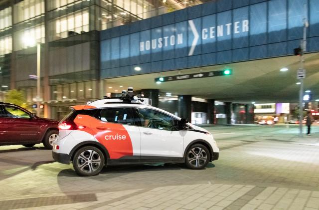 A white car with orange Cruise branding in front of the Houston Center