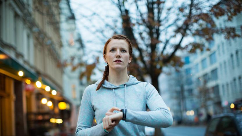 Sporty woman using watch before exercising on sidewalk in city