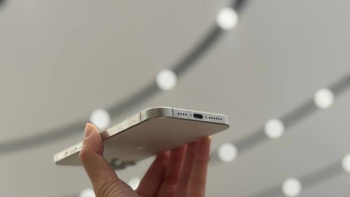 The iPhone 15 Pro Max held up against a ceiling of lights, showing its USB-C port.