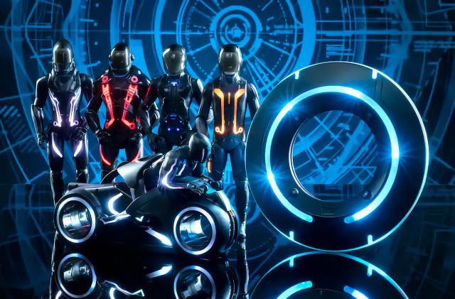 Four Tron action figures (wearing visors) lined up behind a Tron Lightcycle in a futuristic (blue / black) setting.